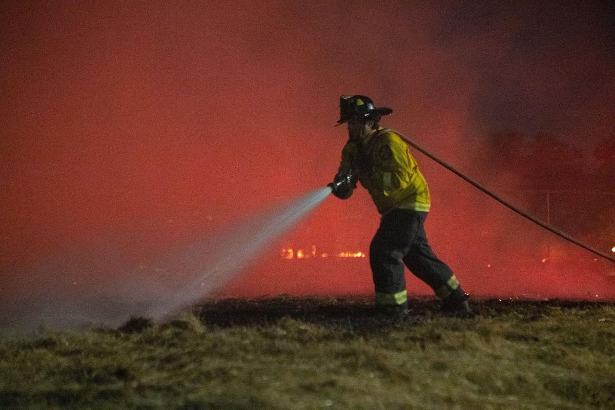 A firefighter douses flames during a vegetation fire along 44th Street in Sacramento in July. Much of the city’s overtime went to personnel in its fire department, according to data obtained through a Public Records Act request.