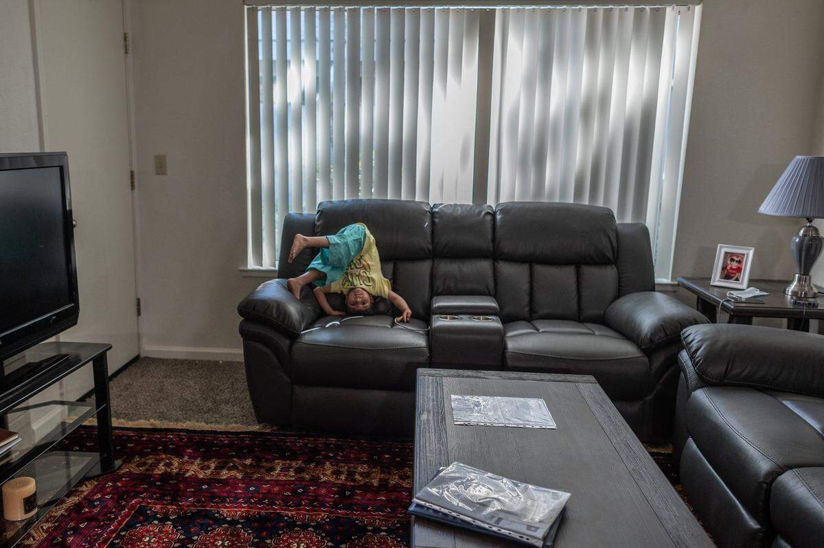 Abdullah bounces on a new couch on Sept. 20 in the living room of a two-bedroom apartment he lives in with his family of eight. In the foreground, a plastic binder holds over a dozen certificates and commendations for his father Abdul, who came to the U.S. on a Special Immigrant Visa after serving as security for the U.S. Embassy in Kabul for 19 years.