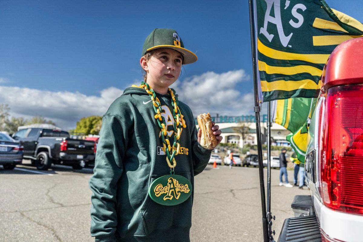 Bailey Jauregui, 12, of Elk Grove, eats a sandwich as she wears an Athletics necklace wit Sacramento printed in the background during the first Major League Baseball game at Sutter Health Park in West Sacramento on Monday, March 31, 2025.