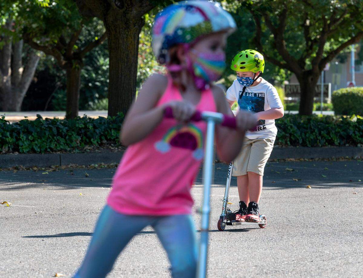 Violette Gottis, left, 7, and, Mason, 9, ride scooters in the Scottish Rite Masonic Center parking lot in East Sacramento on Thursday, July 23, 2020. Mason has chronic health conditions, including Type 1 diabetes and severe asthma, which elevate his risk from COVID-19. His mother plans to keep him out of school until there is a vaccine or more effective treatment.