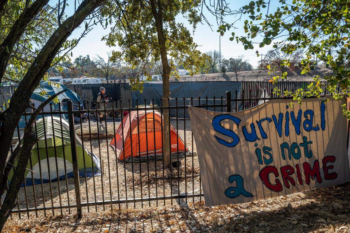 Sharon Jones, who is homeless, walks through an encampment she named “Camp Resolution,” toward her tent on the corner of Arden Way and Colfax Street in Sacramento on Wednesday, Oct.19, 2022. She helped create and hang banners and signs along the fence the city built to create a safe parking lot and place for tiny homes. They never came through on their promise so the homeless reclaimed the lot earlier in this month. “We are humans, we deserve a place to stay,” said Jones.