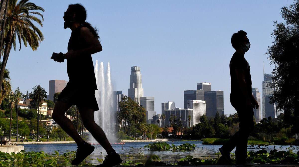 People walk at Echo Park Lake as downtown Los Angeles is seen in the background, Saturday, May 23, 2020, in Los Angeles. California Gov. Gavin Newsom has approved 45 of California’s 58 counties to reopen some businesses since May 8 when he loosened his original mid-March stay-at-home order. (AP Photo/Mark J. Terrill)