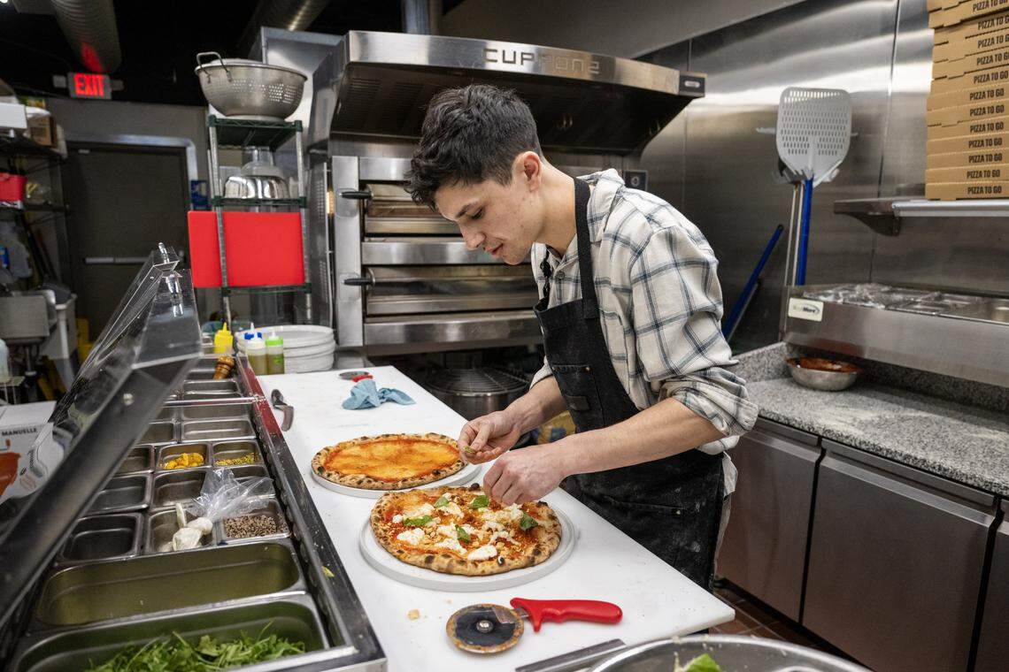 Manager Jackson Wells adds toppings to a pizza order at Dodici Pizza in Sacramento on March 6.