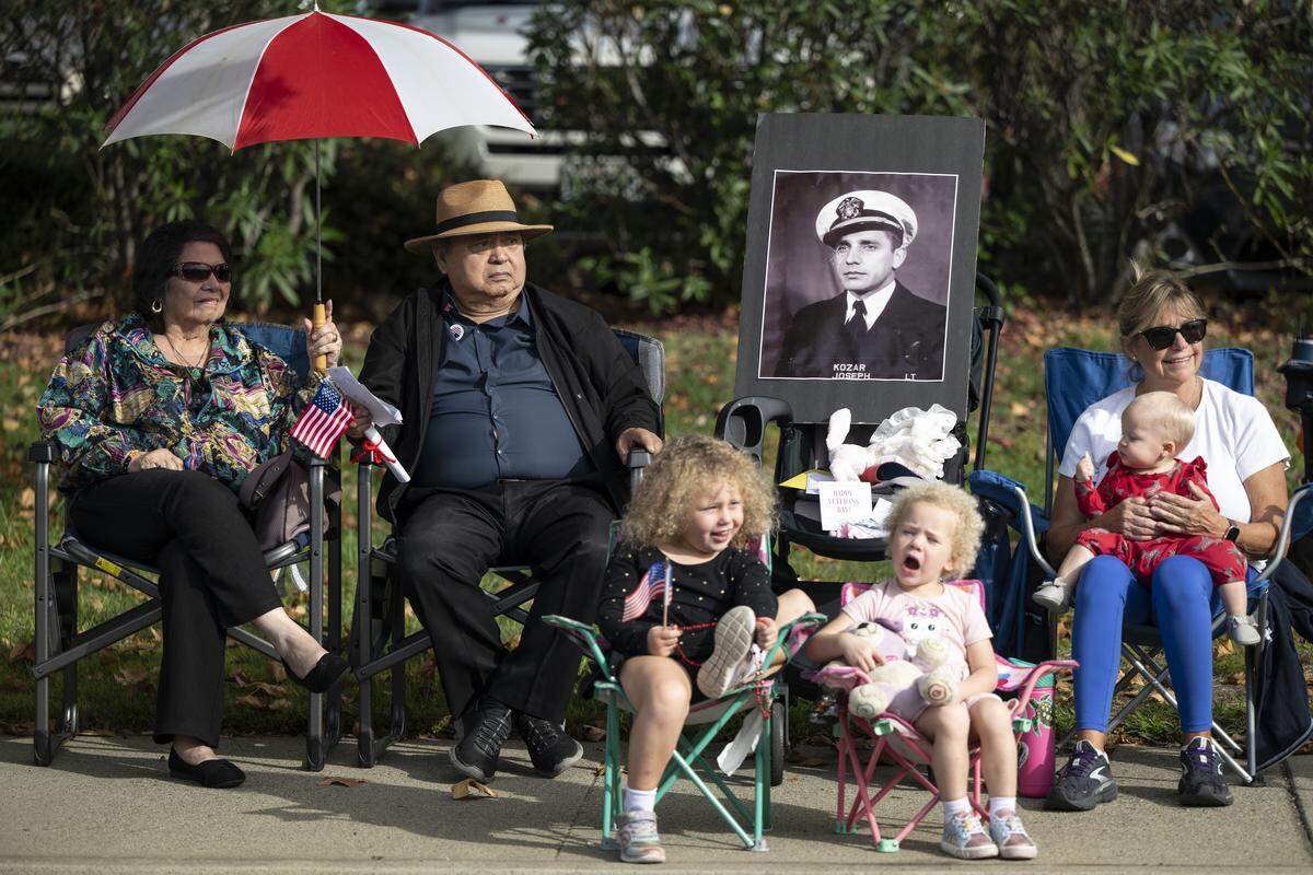Victoria Roberts, right, sits next to a portrait of her father, Joseph Kozar, who was a veteran, during a Veterans Day parade in Folsom on Tuesday, Nov. 11, 2025. Roberts says she brings his portrait to the parade every year.