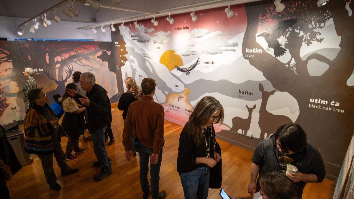 Attendees visiting the ‘Uba Seo: Nisenan Arts and Culture presents ‘The Story of Land, Water, and People’ exhibition in Nevada City, California. The mural features animals and plants with their Nisenan name written alongside.