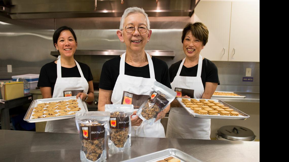 
Tule Yomogida, center, shows packages of the alfalfa honey granola her company, Tule’s Cookies, makes. Her daughter Jennifer Szostak, left, and sister Laura Katayama assist in the business. Szostak holds cranberry almond thins; in the foreground are Hawaiian tiles.
