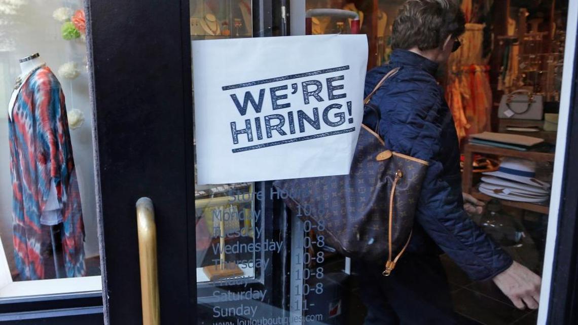 A woman passes a “we’re hiring” sign while entering a Boston clothing store in May. Recent unemployment figures suggested California’s economic recovery is continuing to move forward despite signs of a slowdown on the national level.