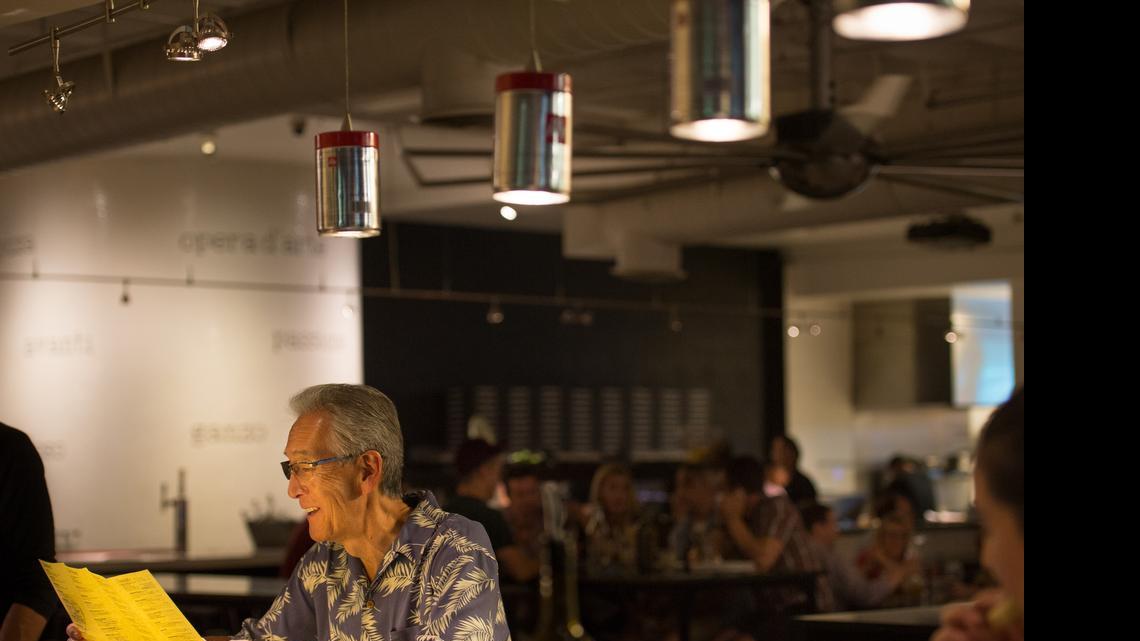 
Gary Kuwabara looks over the menu in May at Hot Italian under lights that have been recycled and repurposed from coffee tins. 
