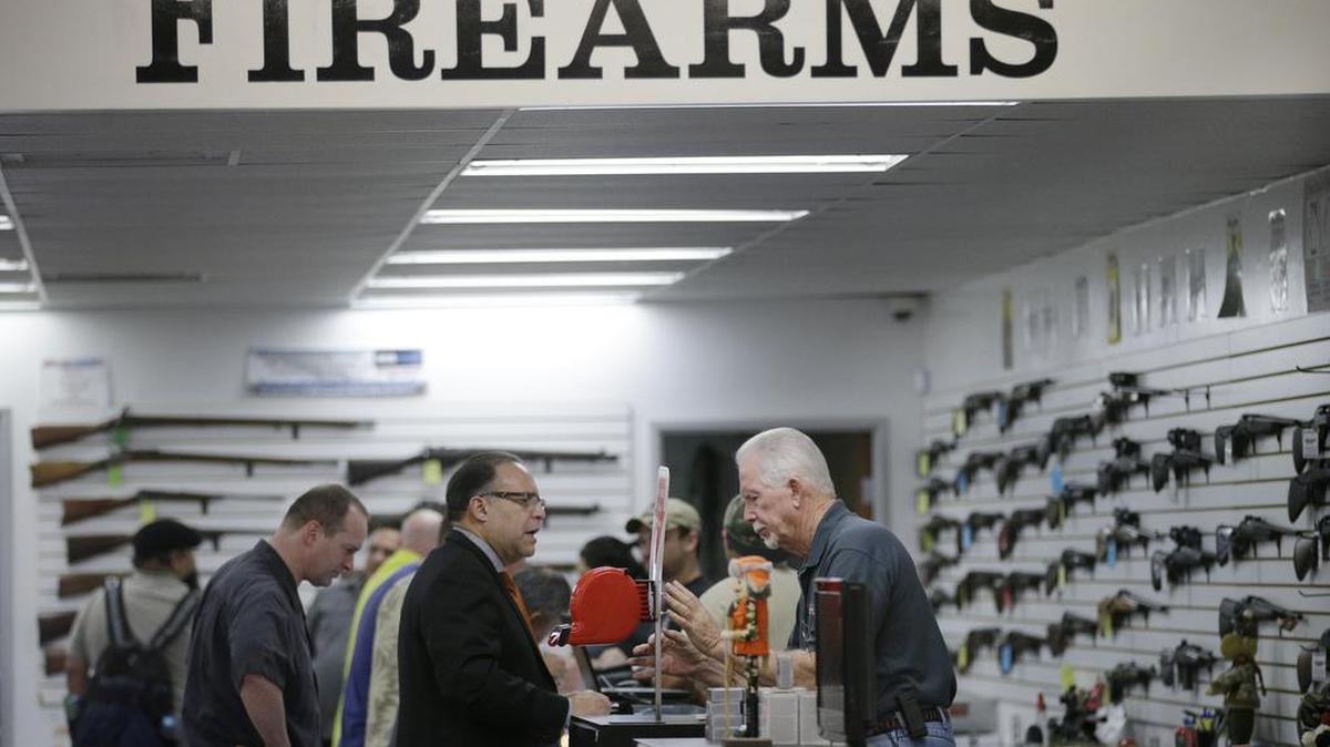 In this Dec. 9, 2015, photo, sales associate Mike Conway, right, shows Paul Angulo a firearm at Bullseye Sport gun shop in Riverside.