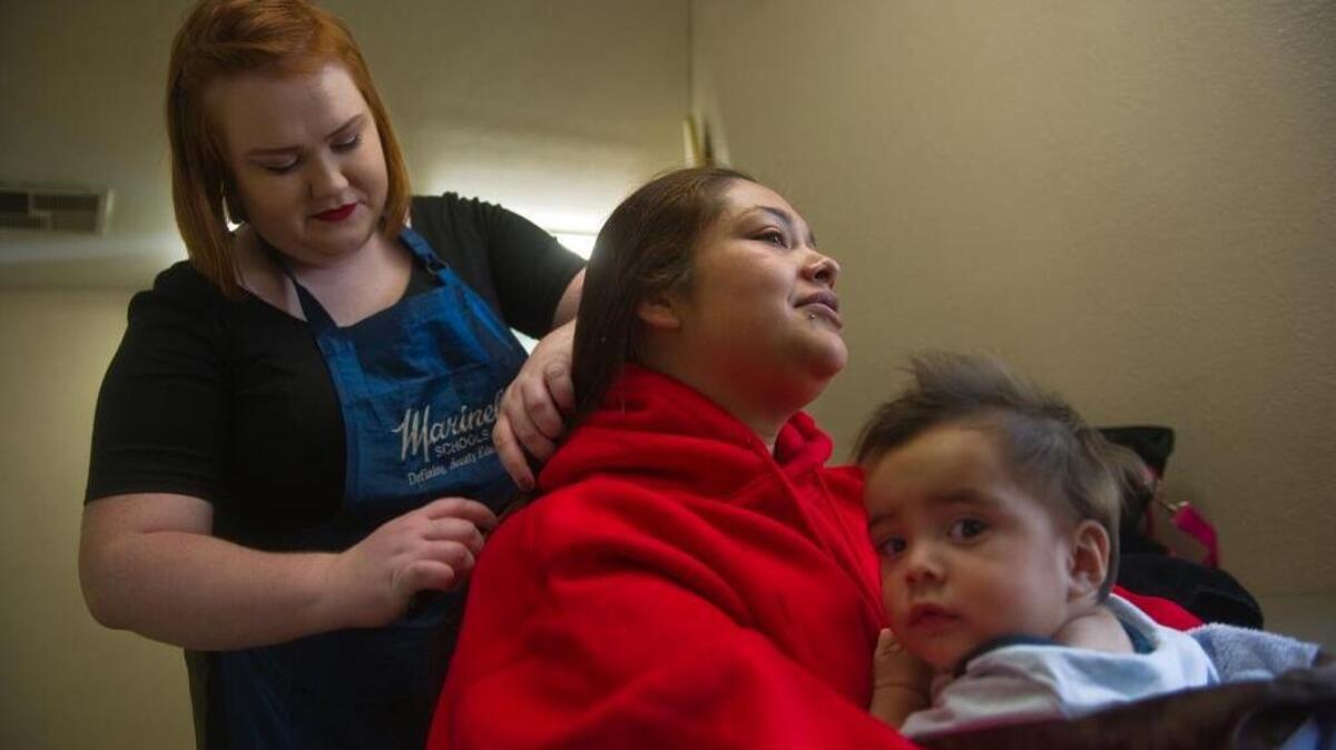 Marinello School of Beauty student Brieann Beath, left, cuts the hair of Angelina Castilla as she holds her 8-month-old sin Josiah at the Help-Portrait event at the Stockton Shelter for the Homeless in Stockton in December 2014. Marinello announced it was closing after federal education officials said they would cut off student loans at some campuses.