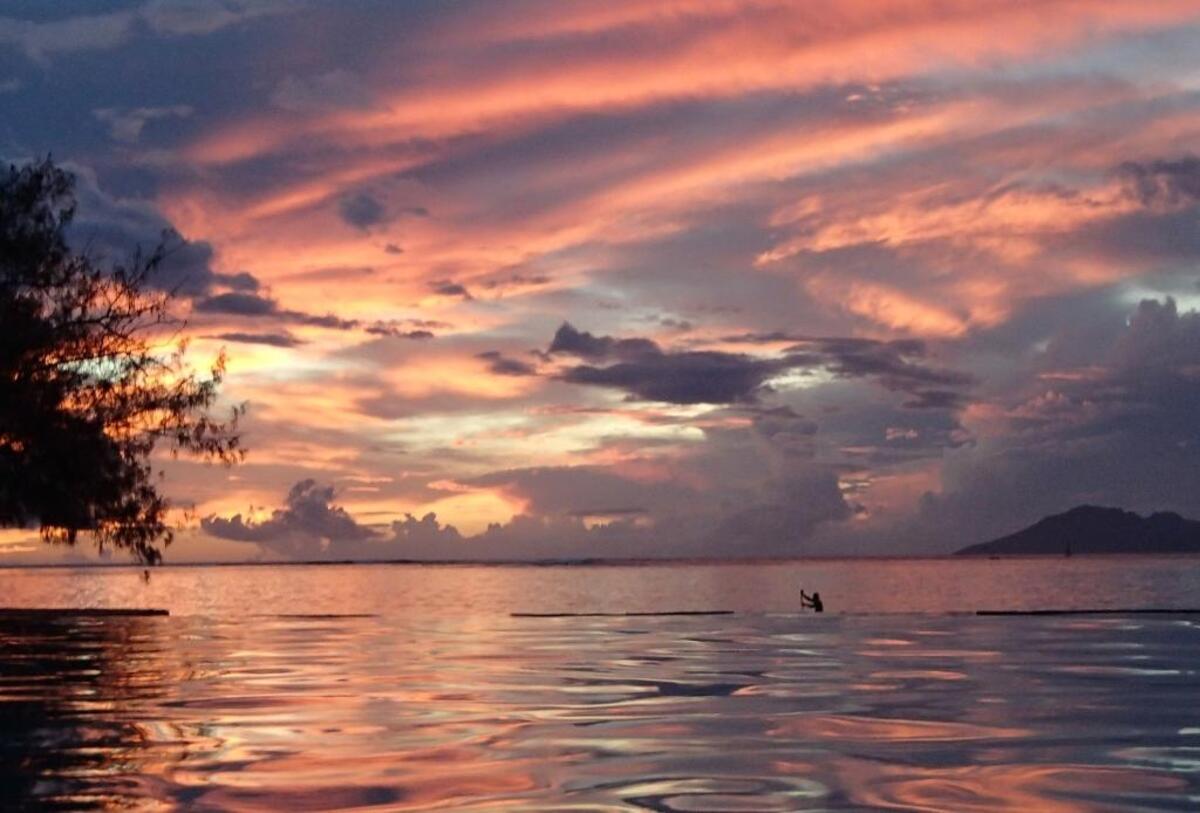 A distant paddler, silhouetted against a fiery sky, becomes part of the story in Papeete, Tahiti.