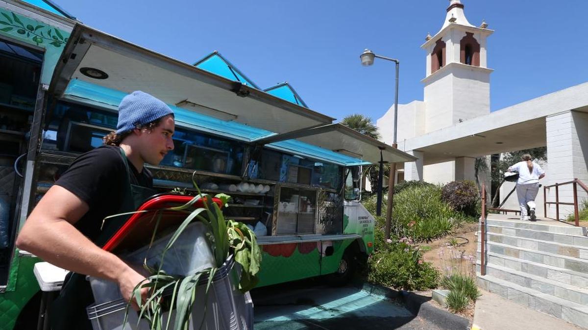 Daniel Lomayesua, 21, assists by carrying fresh produce from a food truck to the St. Francis of Assisi church, background. The northern San Diego County seniors program created by three organizations aims to relieve senior poverty by supplying fresh produce, an inexpensive healthy lunch and camaraderie at this Vista church.