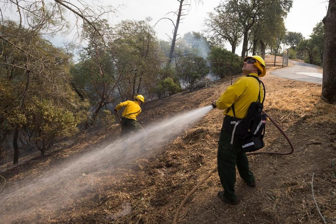 NPS firefighter Chris Corder, right, watches a helicopter drop water on the Pocket Fire as Phillip Lampley protects a home in the Vineyard Development in Sonoma County outside of Geyserville on Wednesday October 11, 2017.
