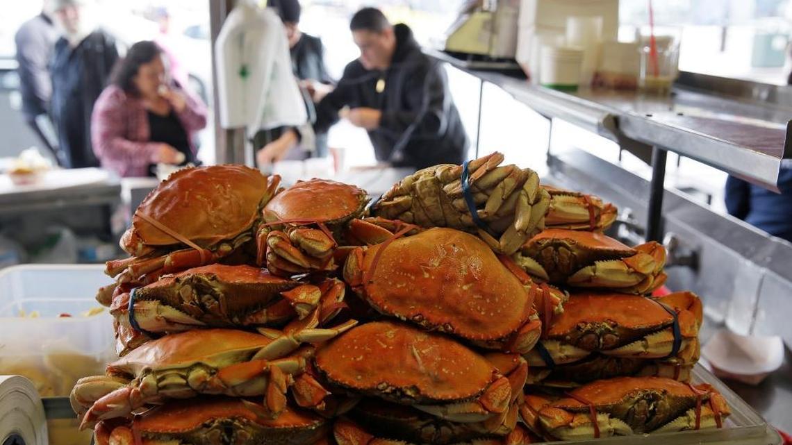 A stack of imported Dungeness crabs are shown for sale as people eat them in the background at Fisherman’s Wharf last December in San Francisco. Though a toxic algae bloom prompted the closure of commercial crab season last year, local crab is expected to be on the menu this year in time for the holidays.