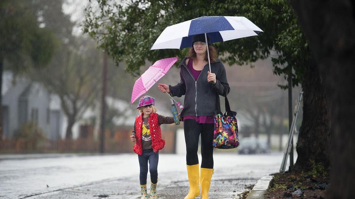 Dressed in rain attire, Rachel Matuskey of East Sacramento walks along C Street near Elvas Avenue with her four-year-old daughter, Mia, after dropping off her brother at school on Tuesday, January 5, 2016, in Sacramento, Calif.