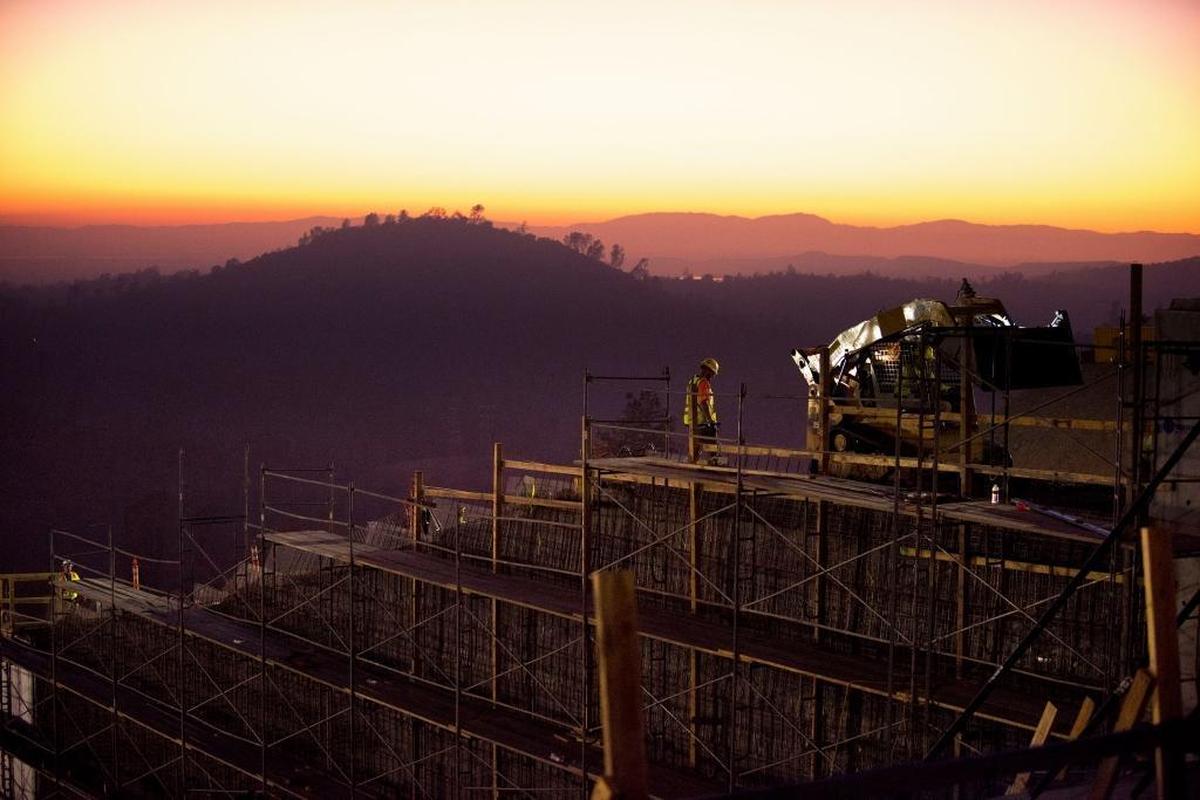 As the sun sets, workers place roller-compacted concrete onto the sidewall between the upper and lower chutes of the main spillway in late October.