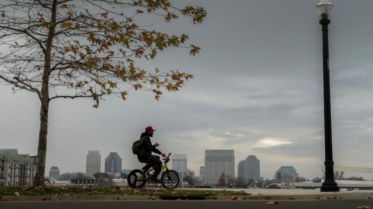 Clouds roll over the Sacramento skyline as a bicyclist rides his bike along Riverine Way in Sacramento.