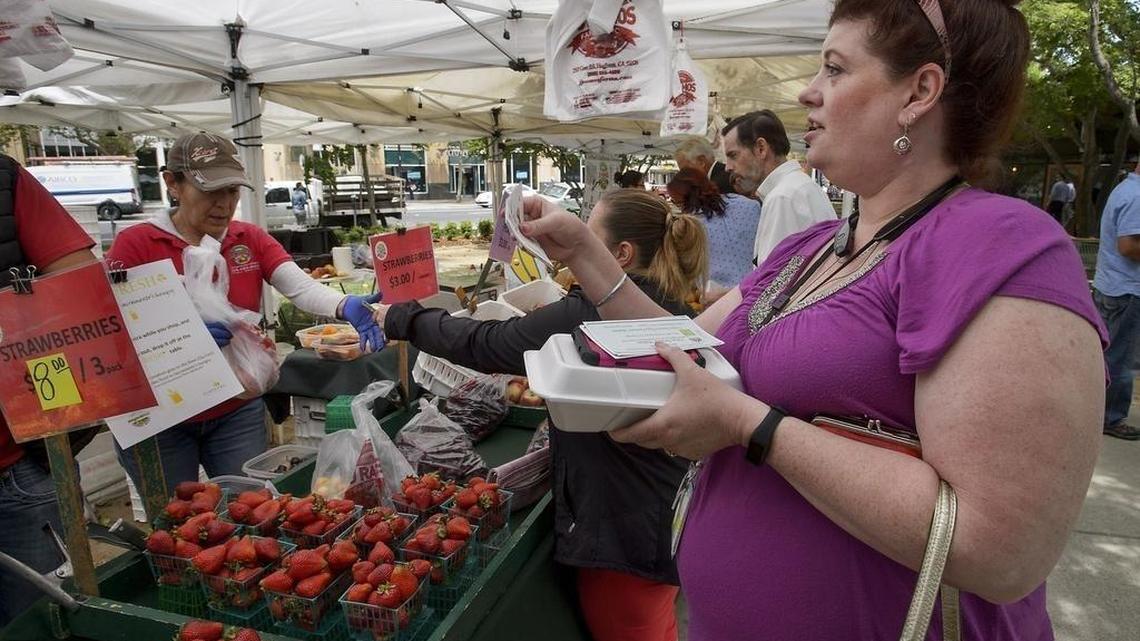 Sandy Nemec of Carmichael, right, buys a bag of cherries with "Market Match" coupons at the Farmer's Market at Cesar Chavez Park in Sacramento on May 24, 2017.
