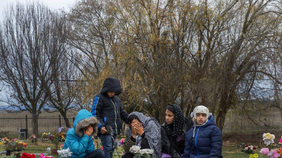 Malalai Rafi and her children grieve  at the Greater Sacramento Muslim Cemetery in December 2015. They lost Mustafi Rafi, husband and father, July 12, 2015, just after arriving in the U.S. on a Special Immigrant Visa. He was killed biking with his son Omar, 8. Omar was gravely  injured. He was released from the hospital in October, and, here, joins his siblings – Saleha,12, Omran, 7,  and Maryam, 13. He wears a helmet to protect  his head, and copes – he was told of his father’s death just days before.