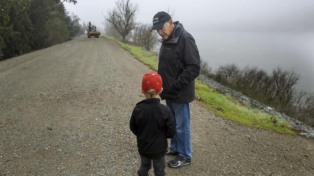 Don Murphy and his grandson Johnny Brewer, 5,  walk the levee at his home in Sacramento in 2018. Murphy’s home is along the Sacramento River, and he owns the levee there. The city voted Tuesday to use eminent domain to take control of the levee behind his home and build a paved bike trail.
