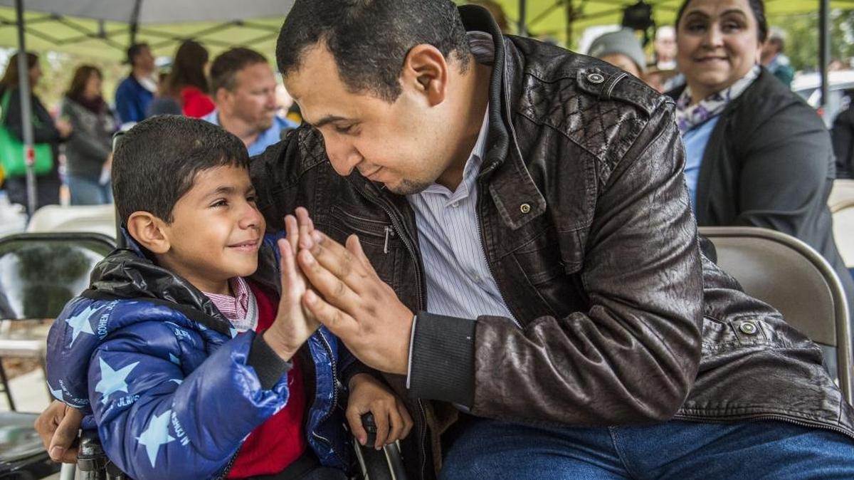 Bassam Mezar comforts his son Mohammed , 7, as they prepare to receive the keys of their new home on Saturday, November 4, 2017. Mezar is a refugee from Iraq.