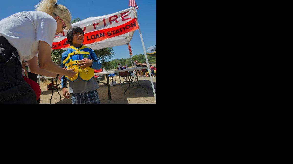 
Brian Parra, 8, of Rancho Cordova gets help from volunteer Betty Taylor as he borrows a free life vest at the Sunrise access to the American River. The American River Parkway Foundation is launching its Kids Don’t Float life vest program two months early due to unseasonably warm weather. Photo taken July 4, 2012 in Sacramento County, California. 
