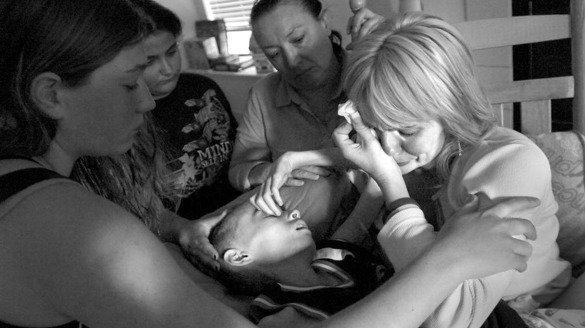 Cyndie French tearfully rocks her dying son Derek, 11, as the song "Because We Believe" plays. Cyndie sings along with Andrea Bocelli in a whispery voice. "Once in every life/ There comes a time/ We walk out all alone/ And into the light..." From left, family friends Ashley Berger, Amy Morgan and Kelly Whysong offer comfort as Cyndie tells Derek, "It's OK, baby. I love you, little man. I love you, brave boy. I love you. I love you."