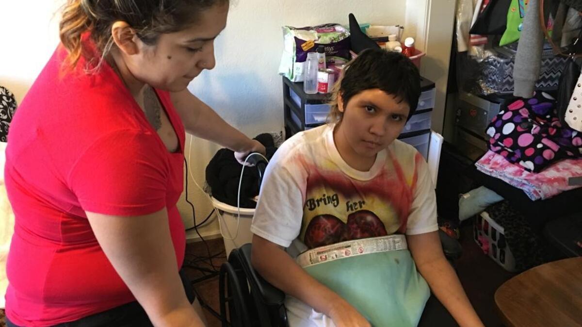 Alize Valadez, 14, spells out words using a paper alphabet chart while her sister, Bianca Valadez, 23, looks on. The teen was shot October 24, 2015.
