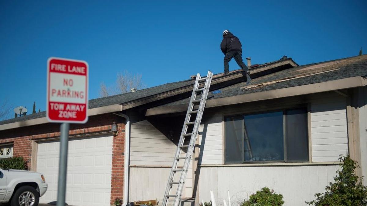 A worker patches up holes on the rooftop caused by a house fire that killed two elderly people and injured a firefighter in the Parkway neighborhood on Saturday in Sacramento.