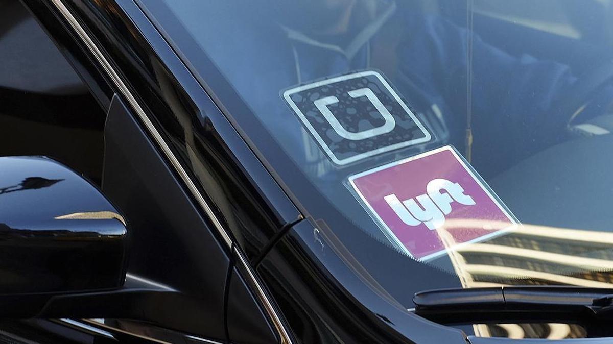 FILE - In this Tuesday, Jan. 12, 2016, file photo, a driver displaying Lyft and Uber stickers on his front windshield drops off a customer in downtown Los Angeles.