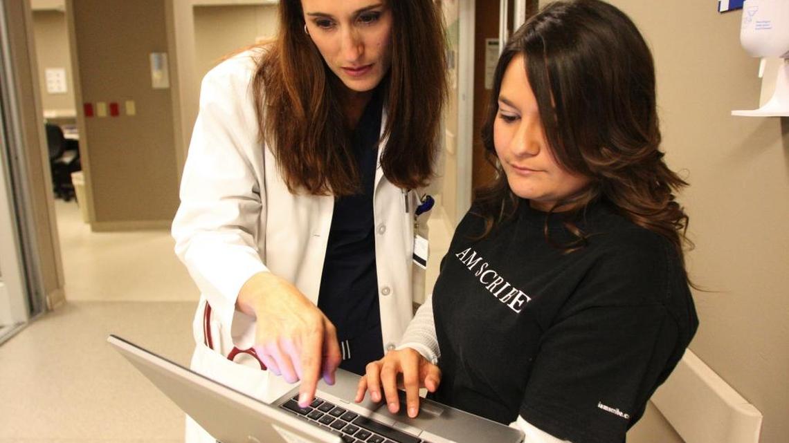 Dr. Marian Bednar, an emergency room physician, left, checks notes with Amanda Nieto, a scribe who works with her, at Texas Health Presbyterian Hospital in Dallas. Scribes have entered the scene in clinics and operating rooms, liberating physicians from the constant note-taking that modern electronic health records systems demand.