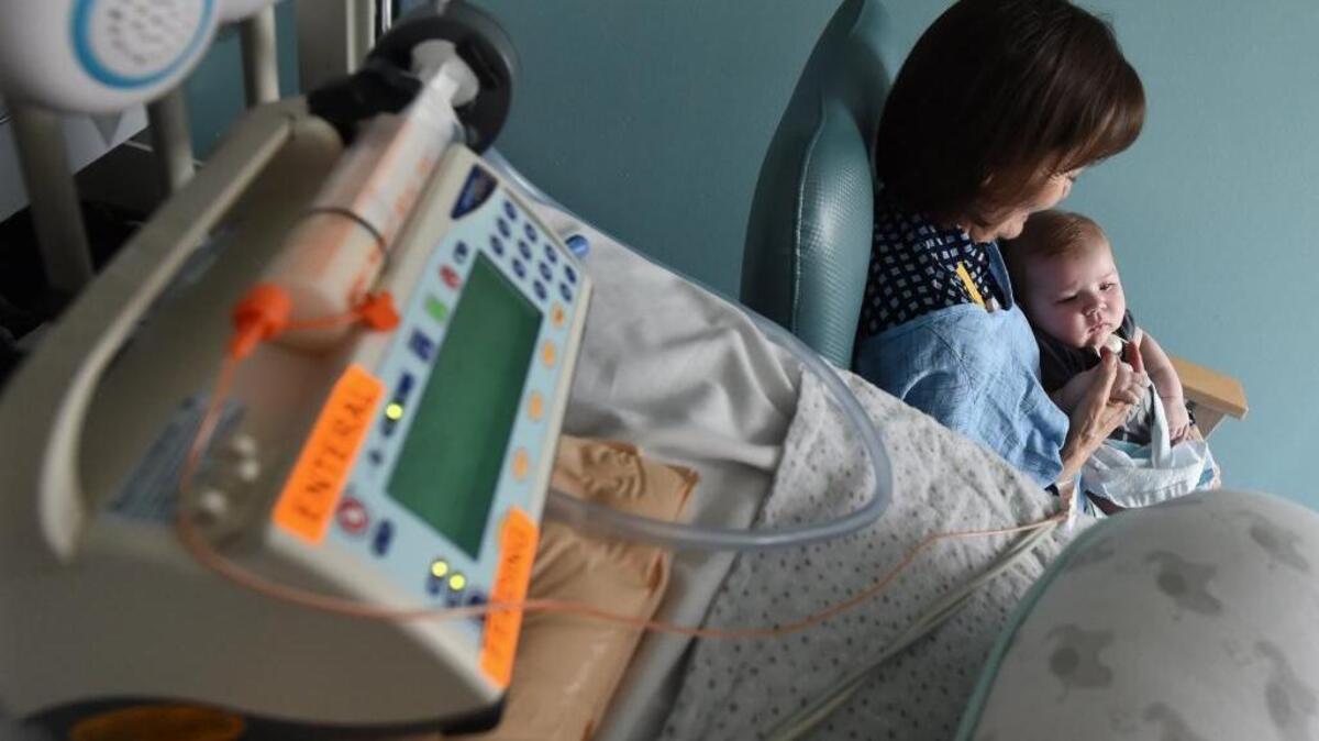 Valley Children’s Hospital volunteer cuddler Kerry Abbott cuddles Grant Early, nearly 4 months old, in the neonatal intensive care unit, as medical equipment he’s hooked up to sits nearby.