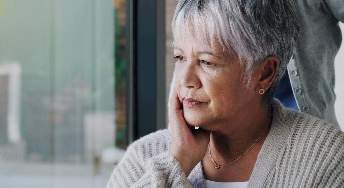 An older woman looking concerned looking out a window.