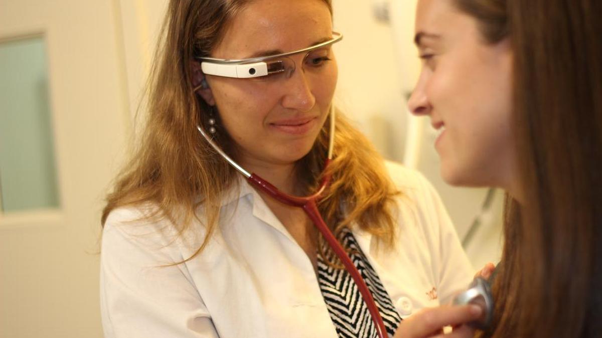 Doctor wearing Google Glass eyewear while examining a patient. Google Glass-powered service from Augmedix Inc. touted as an electronic health records breakthrough, giving doctors more face time with patients.