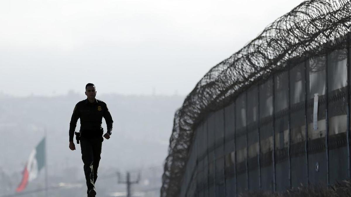 Border Patrol Agent Eduardo Olmos walks last summer near the secondary fence separating Tijuana, Mexico, background, and San Diego in San Diego. A Homeland Security document says the department has identified three spots – including land near El Centro in Imperial County – where it will construct a wall to replace a border fence.