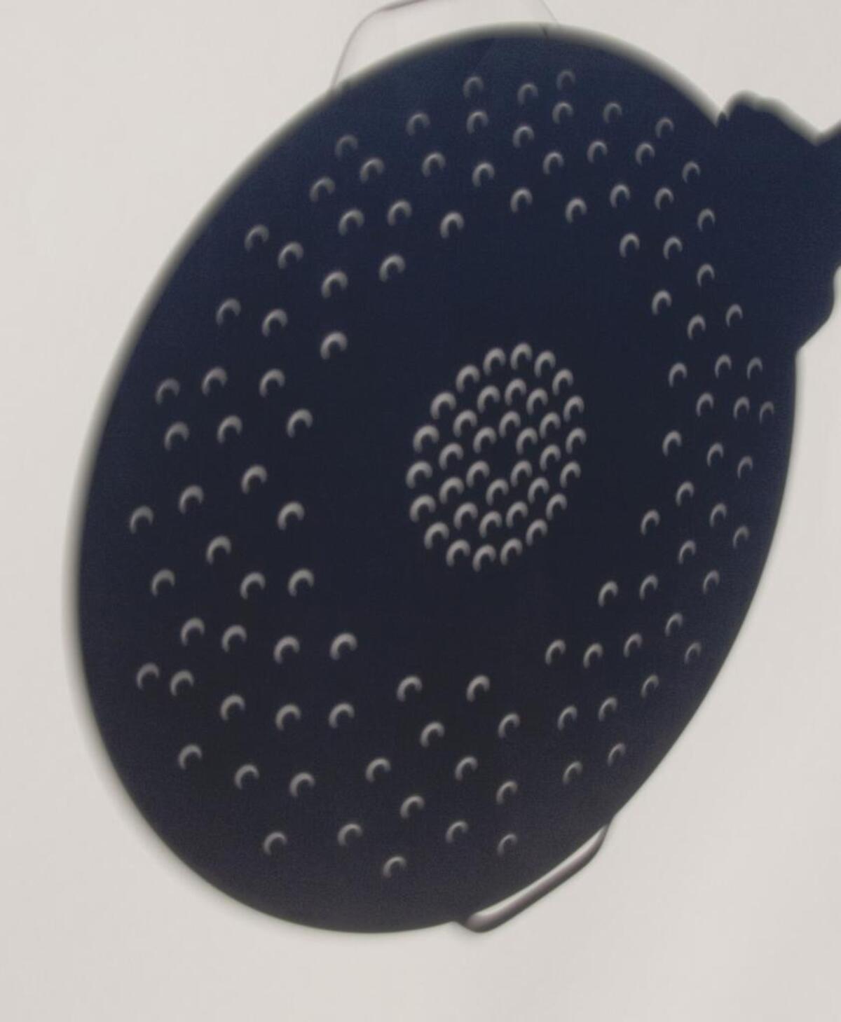 The distinctive shadows of a partial eclipse seen through the holes of a colander.