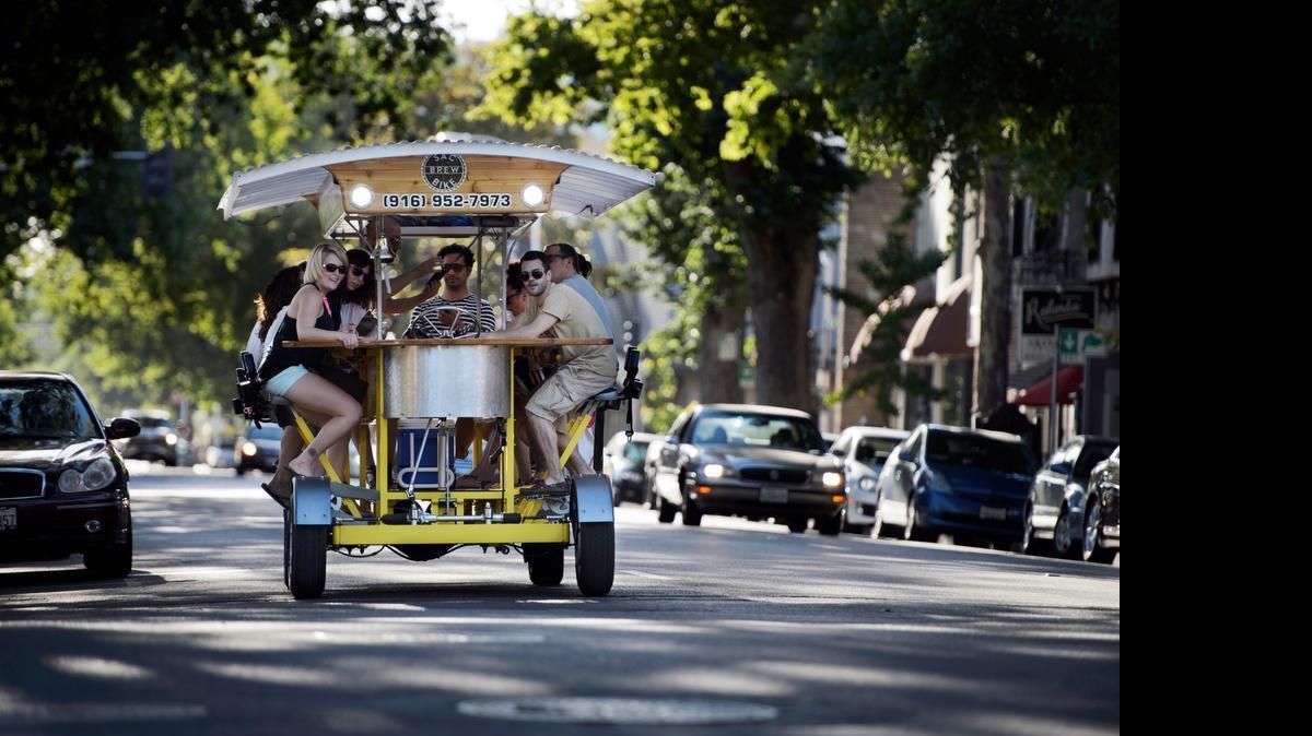 
Sac Brew Bike owner Chris Ferren-Cirino, right, steers the16 passenger bike down J Street after a stop at Kuprows Craft House on May 25, 2014 in midtown Sacramento. Chelsea Irving, from left, and Megan Sullivan pedal to music blasting though the sound system. The Sac Brew Bike is a eco-friendly cycle that fits fifteen passengers and one driver. The business plans to open a bar on 19th Street.
