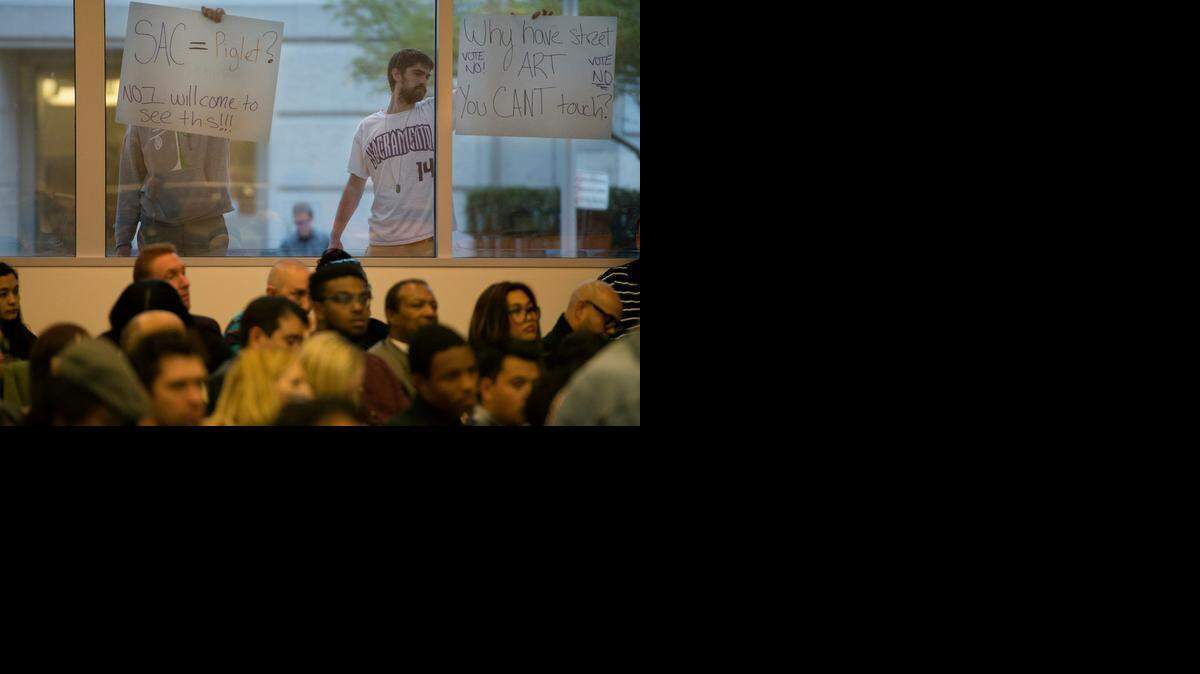Robb Swanson, right, and Doug Wilson hold posters opposing the sculpture chosen to go in front of the arena Tuesday at the Sacramento council meeting.