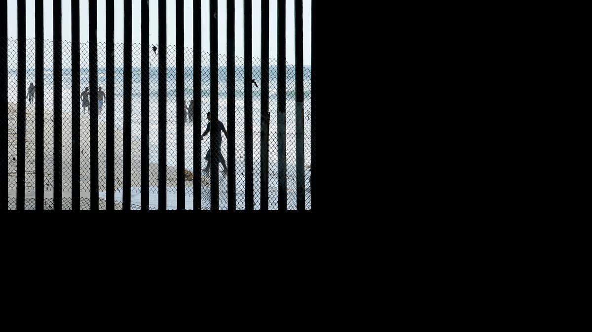 
People walk along the beach in Tijuana, Mexico, where metal bars marking the border with the United States at the sea. 
