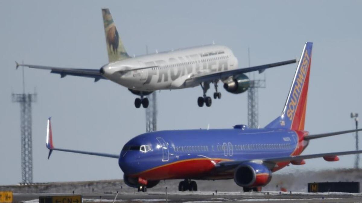 In this photograph taken Feb. 8, 2016, a Southwest Airlines plane, front, waits to take off from a runway as a Frontier Airlines plane lands at Denver International Airport.
