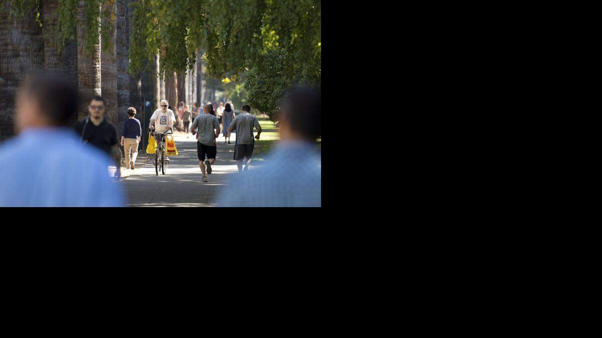 A bicycle rider mixes with pedestrians on an L Street sidewalk next to Capitol Park in downtown Sacramento, creating a potentially dangerous situation.