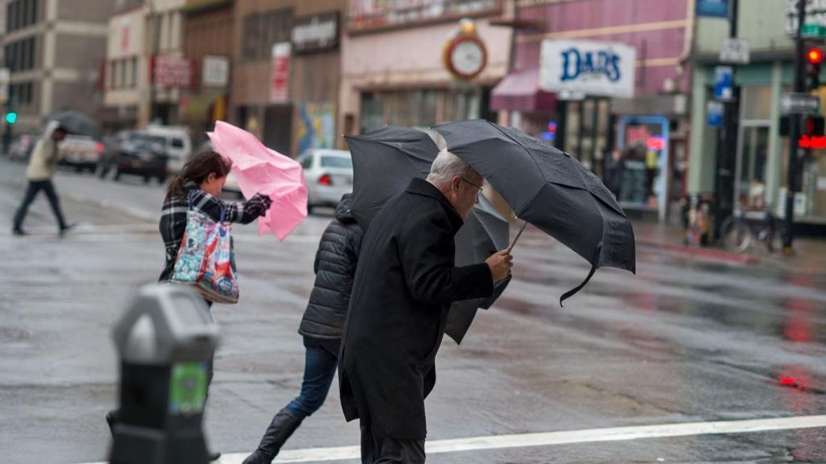 Pedestrians fight back wind and rain while crossing J Street in downtown Sacramento in December.