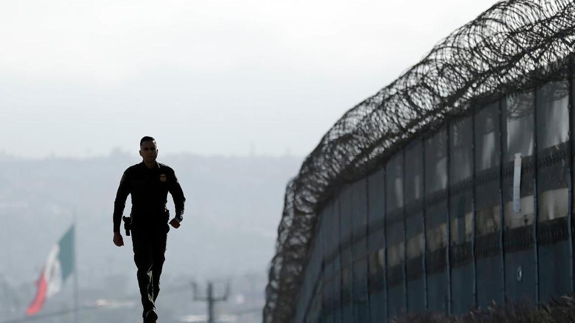 A Border Patrol agent walks on the U.S. side of a fence separating Tijuana, Mexico, background, and San Diego.
