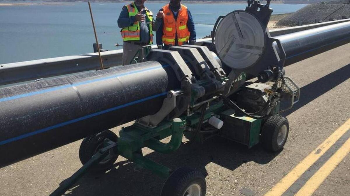 
Workers inspect pipes along the top of Folsom Dam that will connect to a floating pumping barge. U.S. Bureau of Reclamation.
