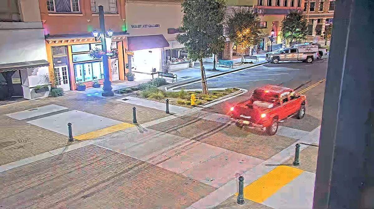 A bright red pickup truck passes through a deserted pedestrian walkway in front of several storefronts not even 30 seconds before the sneaky creature darts out into the street.