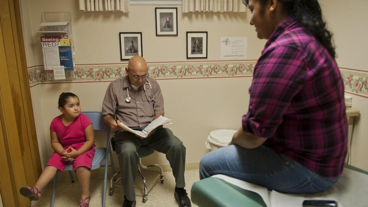 Dr. Douglas Tolley, center, reads the chart of Medi-Cal patient Lucia Trejo-Perez as her daughter waits. Tolly says 70 percent of his patients are Medi-Cal recipients.