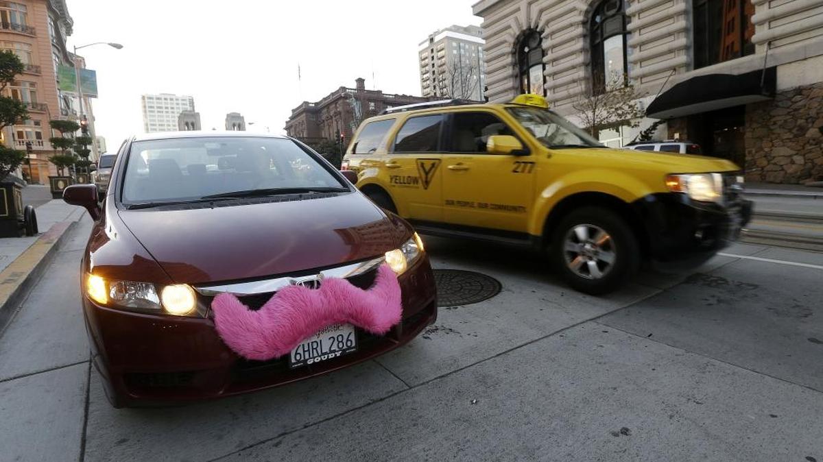 A Lyft driver waits in her car after dropping off a passenger as a taxi cab passes her in San Francisco.
