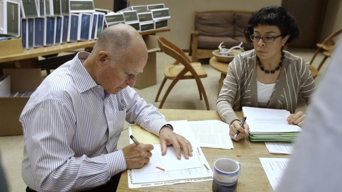 
California Gov. Jerry Brown signs one of the hundreds of bills he had left to deal with as Graciela Castillo-Krings, right, his deputy legislative secretary, looks on at his Capitol office on Friday Oct. 9, 2015. 
