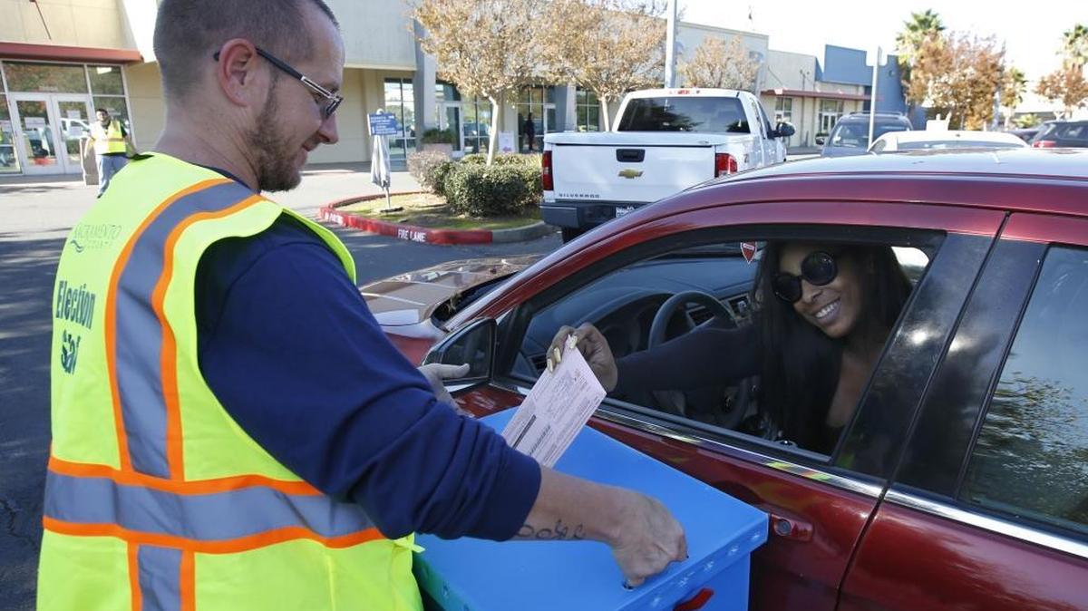 Election worker Michael Vanderpool takes the ballot from Jordyn Daniel at a drive-by location at the Sacramento County registrar of voters office in Sacramento on Tuesday.