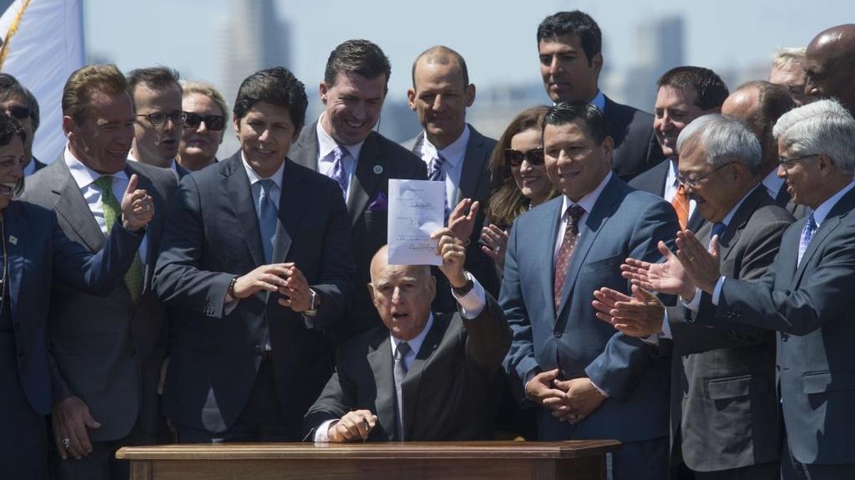 Gov. Jerry Brown raises the signed bill extending the cap-and-trade climate change program until 2030 on July 25, 2017 in Treasure Island.